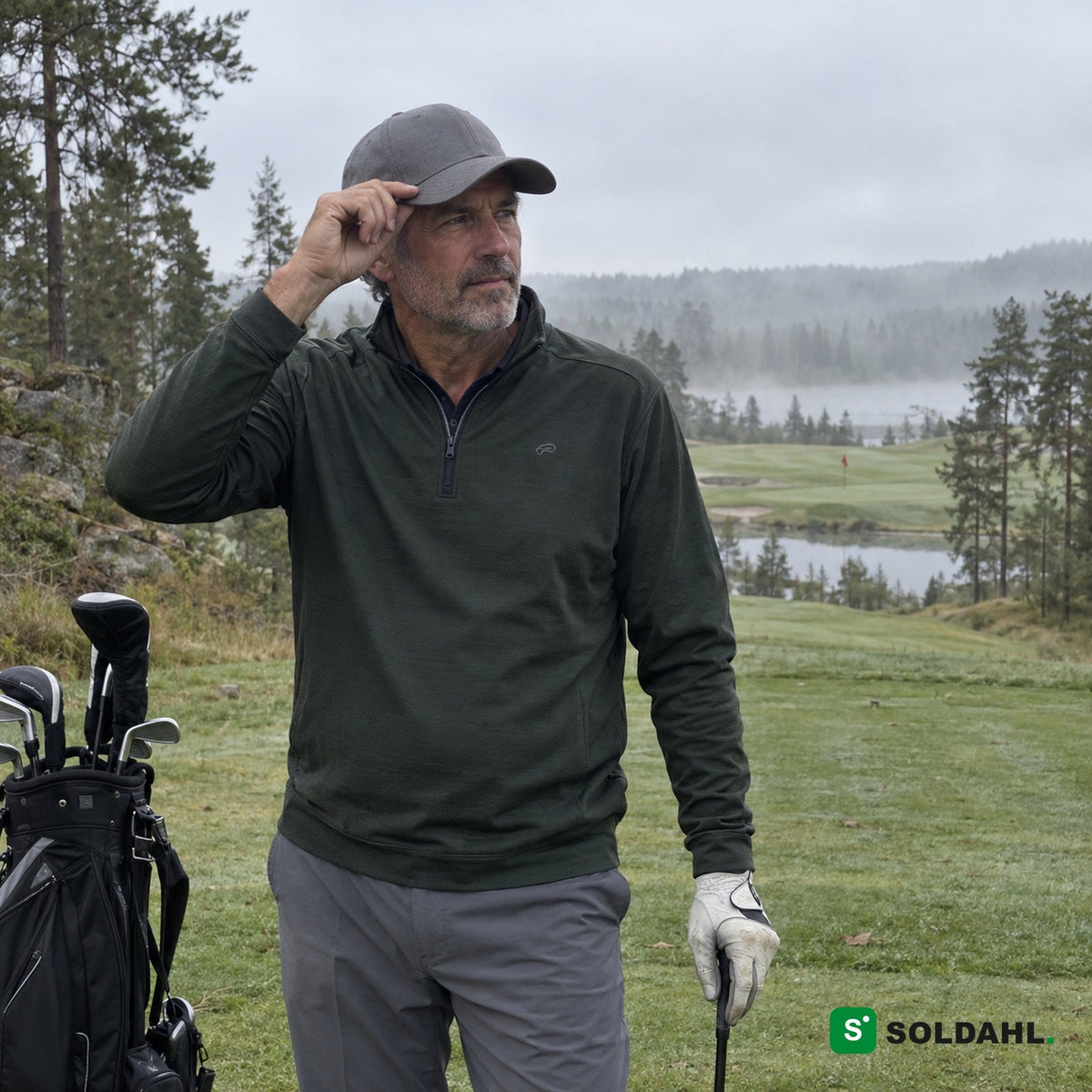 Vihreäpaitainen golfaaja säätää harmaata lippistä sumuisella golfkentällä